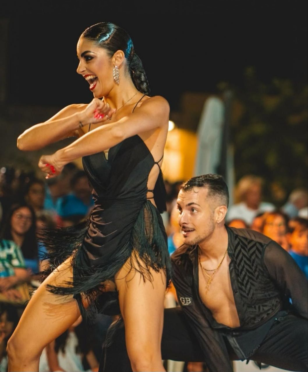 Donna in abito nero con frange e uomo ballano con passione, spettacolo serale all'aperto.