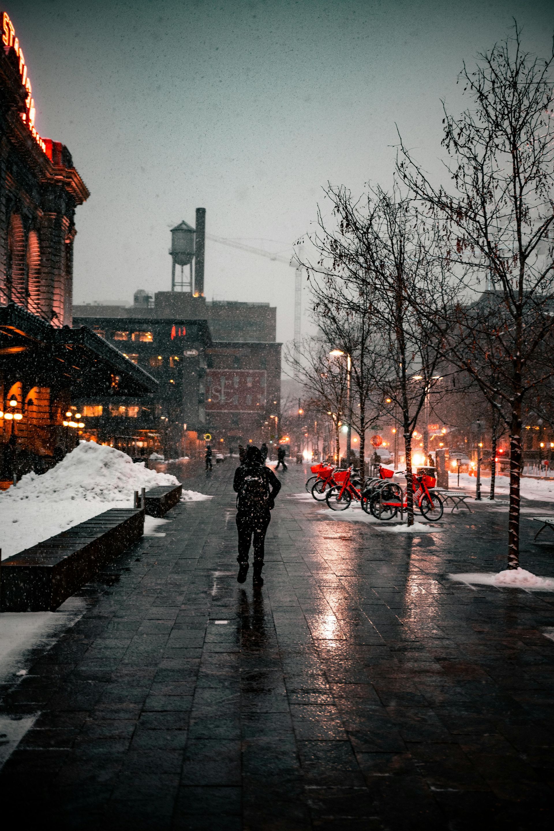 Snowy city street scene with a person walking, red bikes, and buildings.