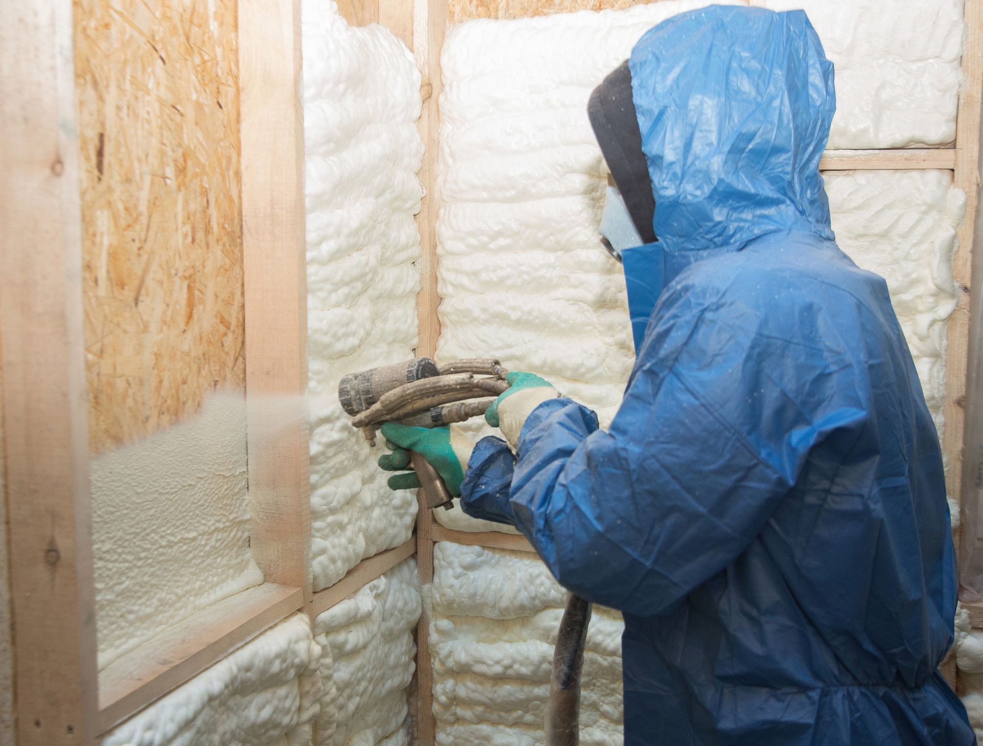 A man is spraying foam insulation on a wall.