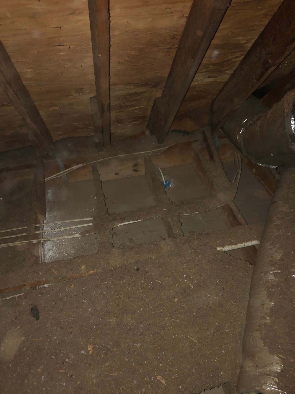 A dirty attic with a wooden ceiling and a metal pipe.
