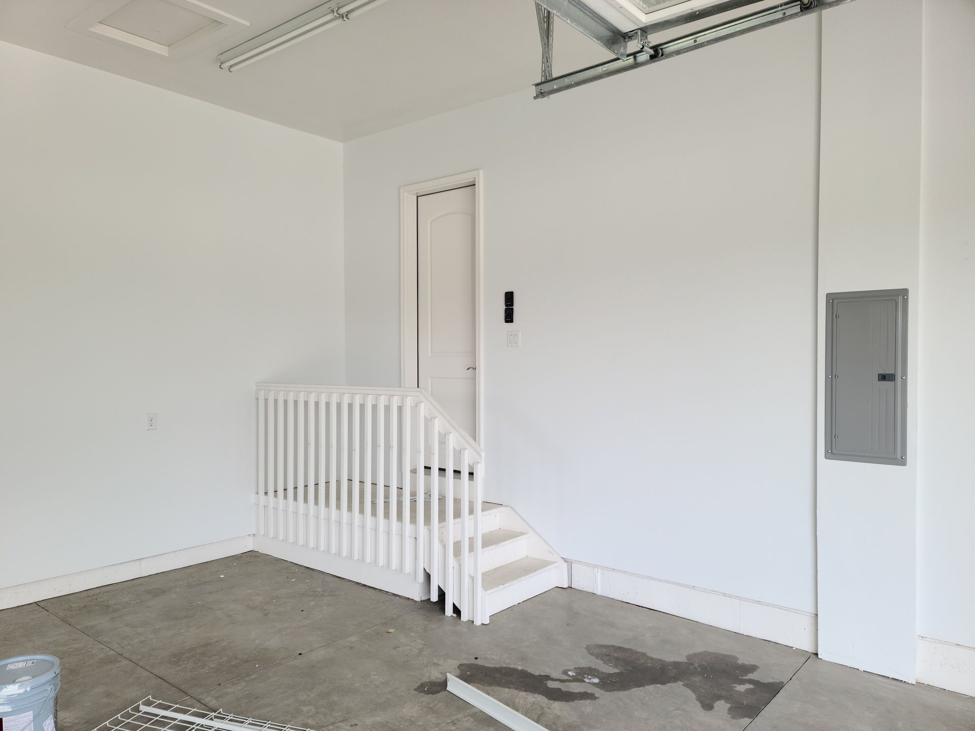White garage interior with stairs, door, and electrical panel on wall.