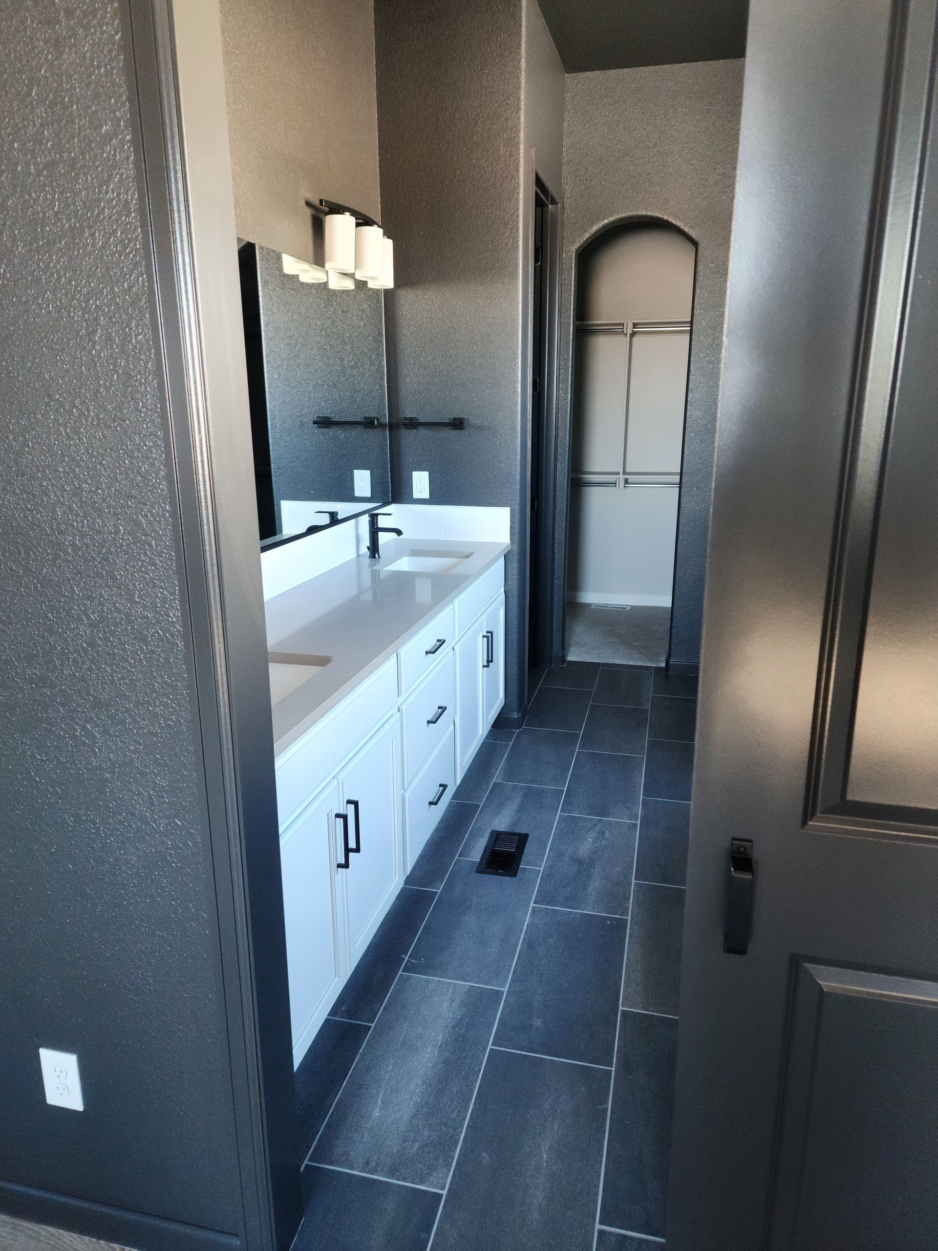 Bathroom with white vanity, black hardware, dark gray walls, and tile floor leading to a shower.