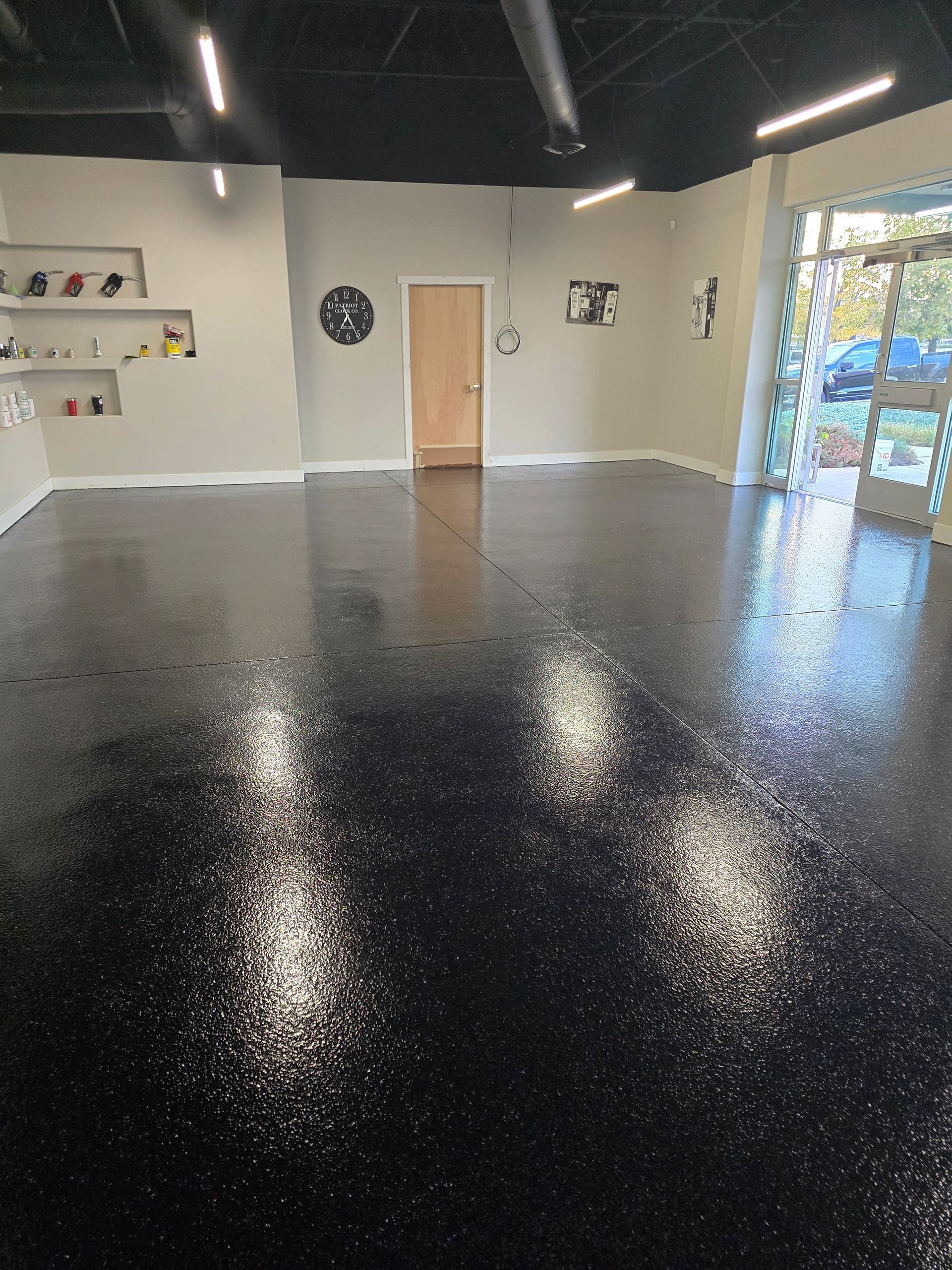 Room with shiny black epoxy floor, white walls, and a black ceiling; a door and a window are visible.