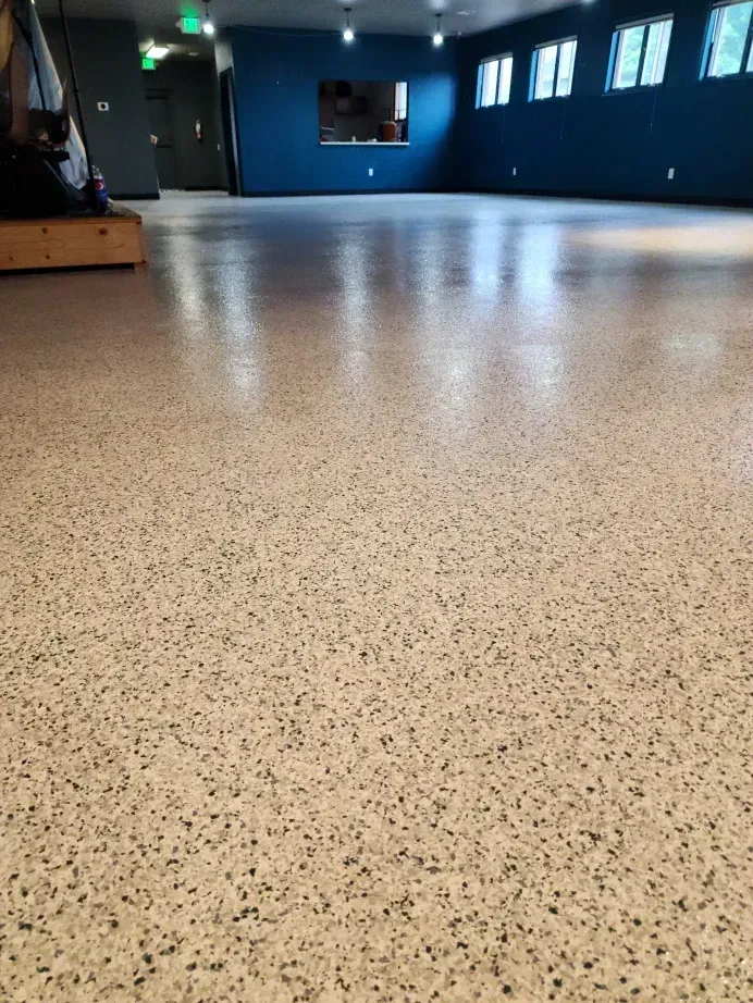 Empty room with speckled beige floor, blue walls, and windows.