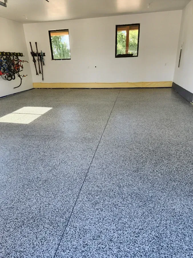 Garage interior with a gray speckled epoxy floor, white walls, and two windows.