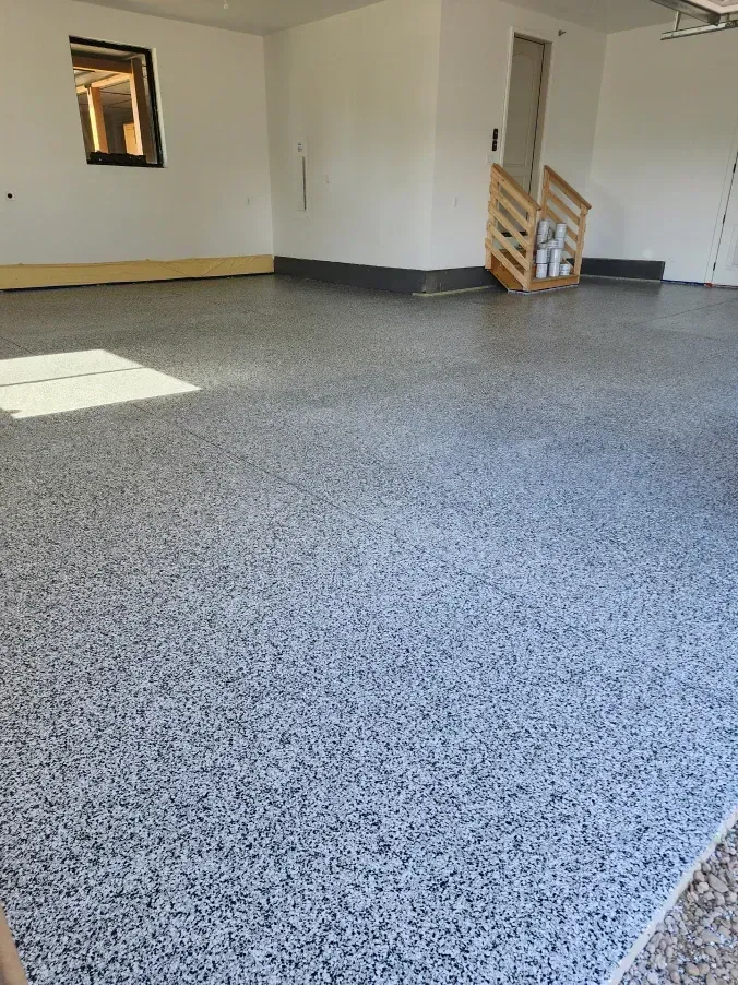 Garage with speckled, gray concrete floor. White walls and small window.