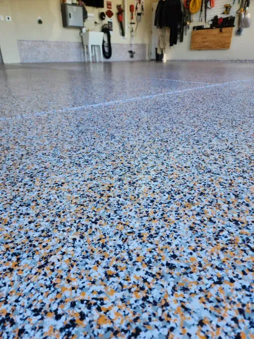 Epoxy garage floor with blue, orange, black flecks. Tools and storage in the background.