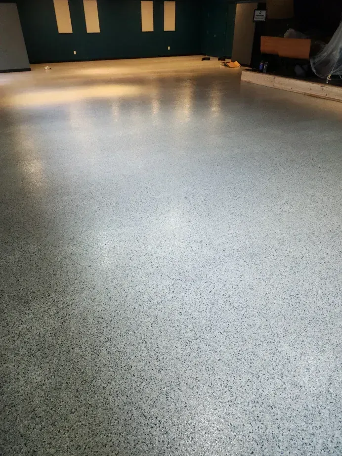 Polished gray concrete floor in an empty room, reflecting light. Teal wall with square cutouts in the background.