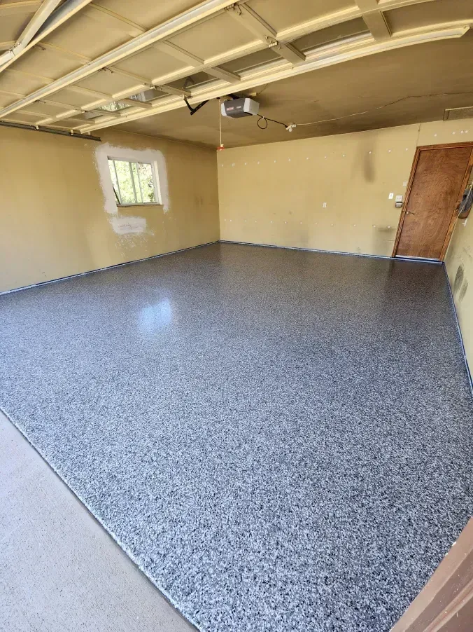 Garage with newly coated floor, gray speckled pattern. Yellow walls, tan ceiling. Window and brown door visible.