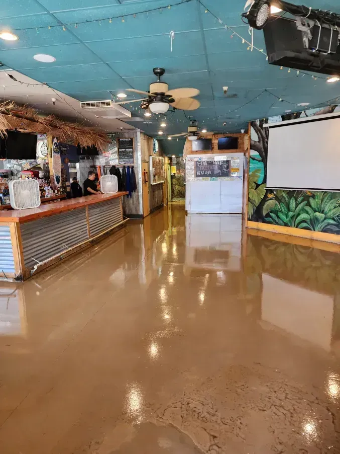 Interior of a bar with a reflective brown floor and a counter with people. Turquoise ceiling.