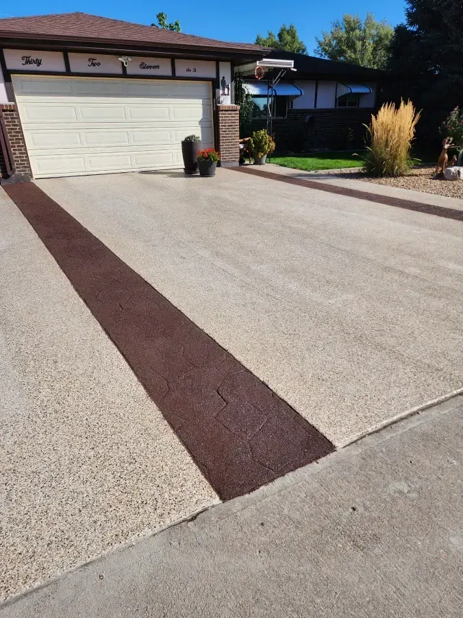 Driveway with textured brown stripe down the center. Garage door and house in background.