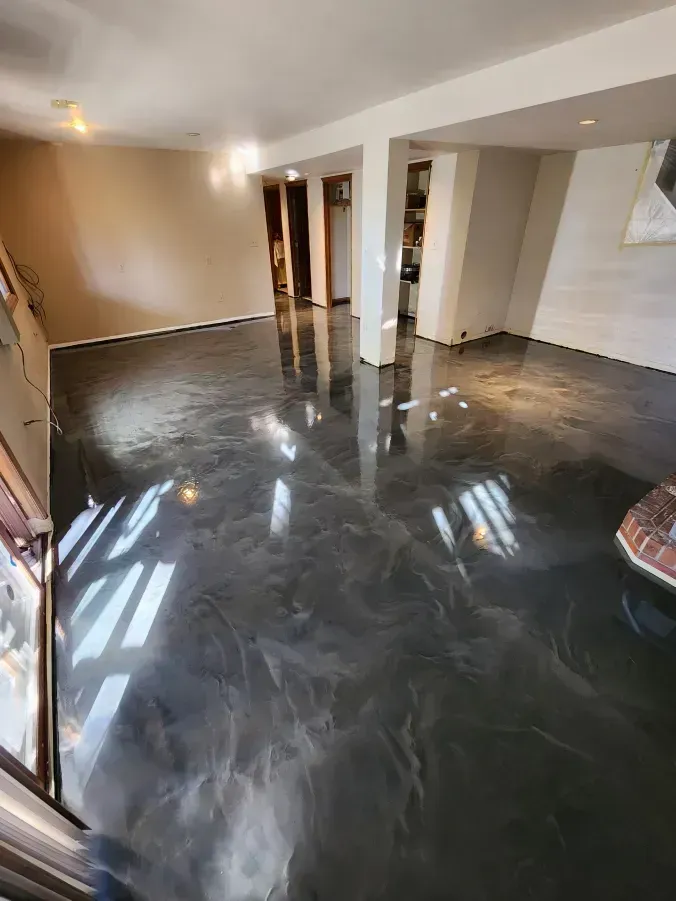 Dark, glossy epoxy floor in a room, reflecting light and surroundings.