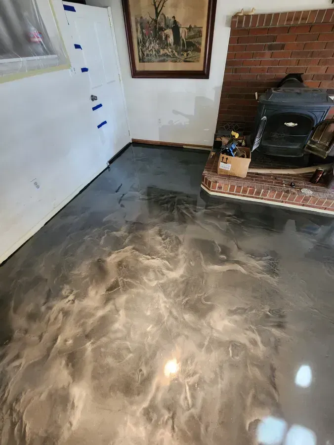 Metallic epoxy flooring in a room with a fireplace and white walls. Silver and gray swirls reflect light.