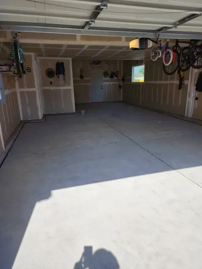 Empty garage with light gray concrete floor and drywall walls; two bikes hanging.