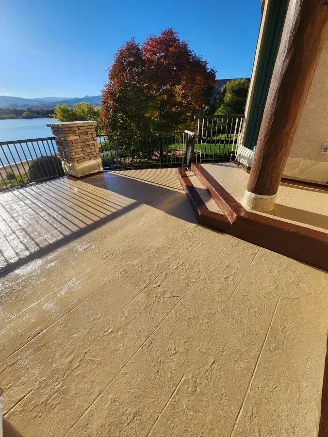 Exterior deck with stamped concrete, railing, lake view, and autumn tree.