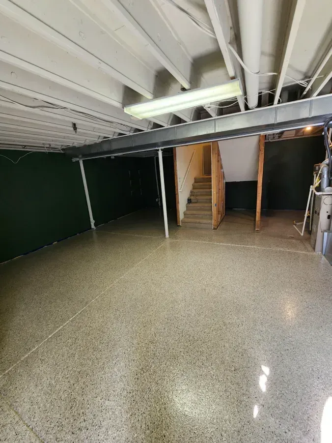 Basement with polished concrete floor, green wall, exposed beams, and stairs.