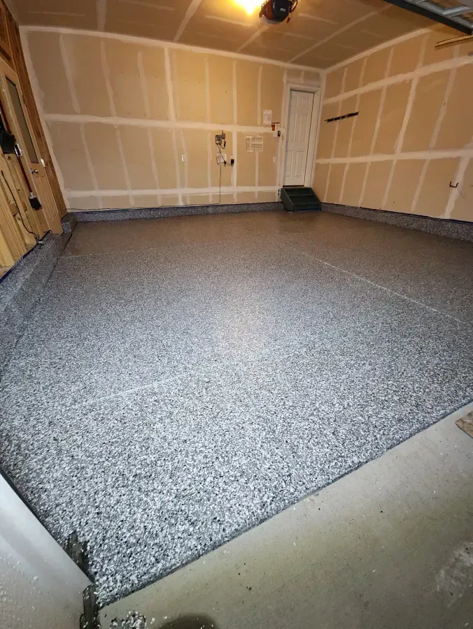 Garage with a speckled gray epoxy floor, tan walls, and a white door.