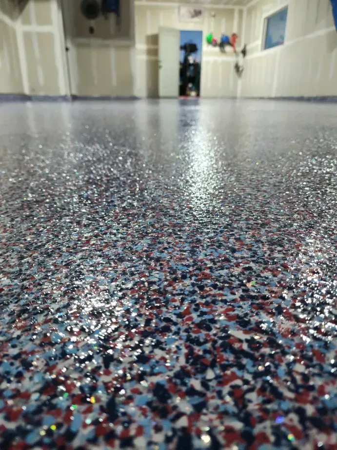Close-up view of a garage floor with a shiny, speckled epoxy coating in blue, red, and silver.