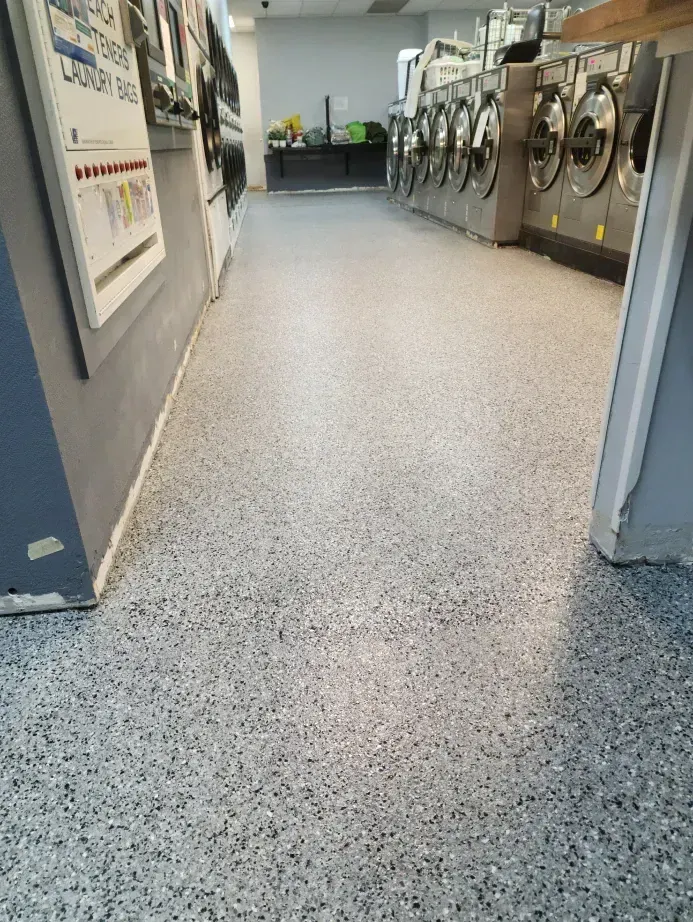 Laundry room with a speckled gray floor, washers, and a counter in the background.
