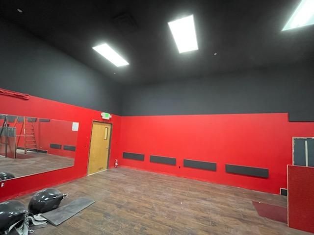 Empty red-walled room with black ceiling and wood floor. Mirror on left, door in middle.