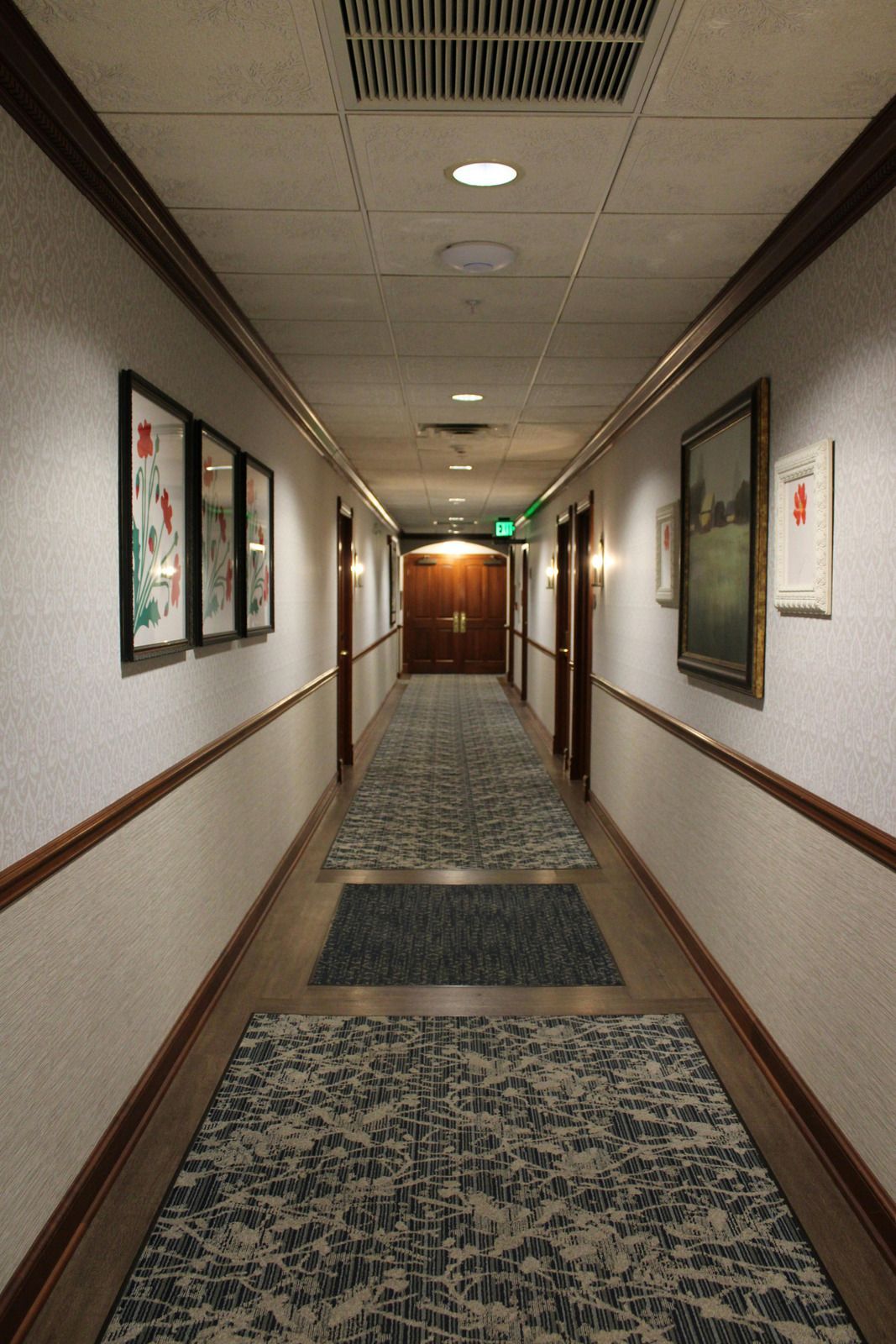 Hallway with patterned carpet, white walls, wood trim, closed doors, and artwork.