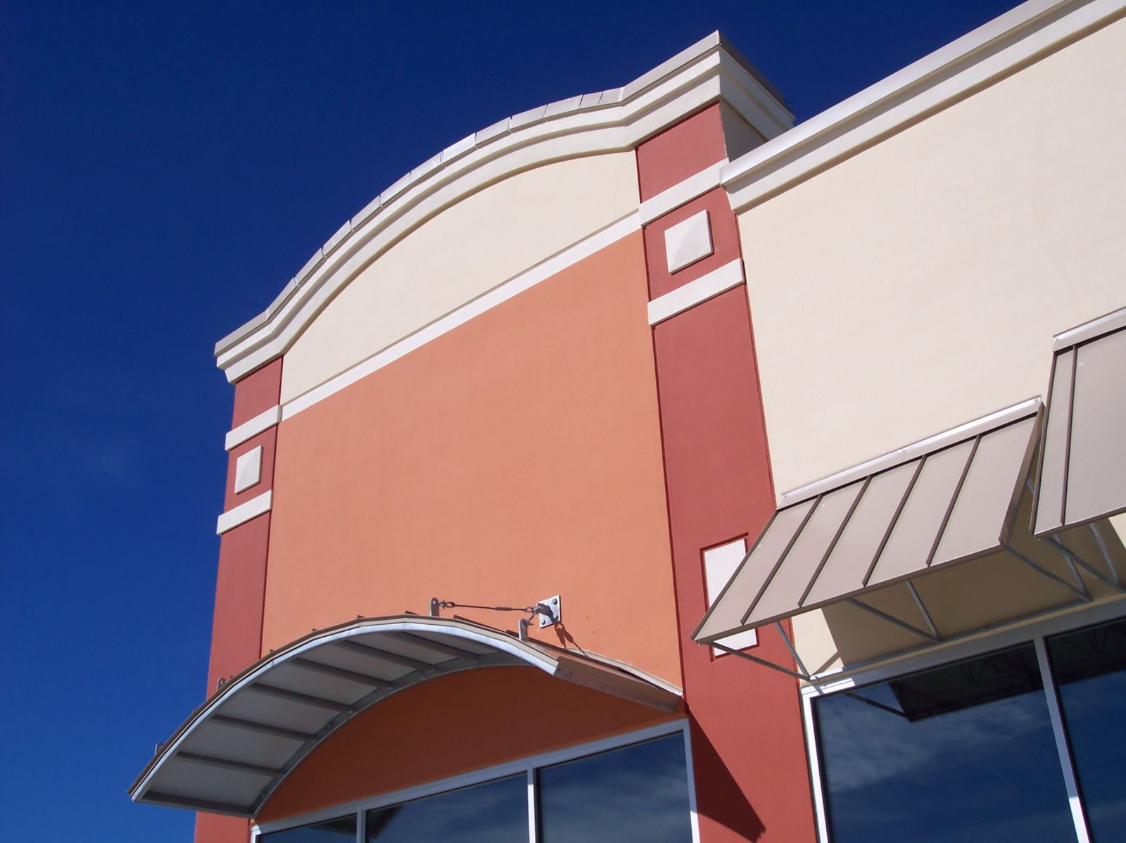 Exterior of a commercial building with peach and red walls, a white awning, and blue sky.