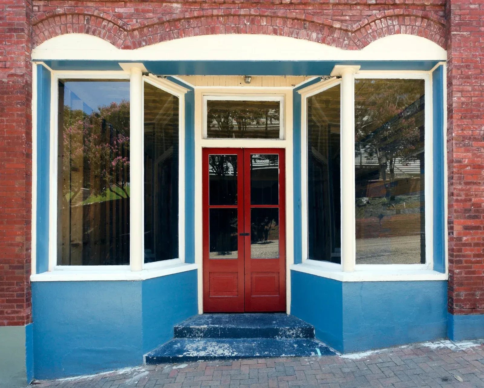 Red door, flanked by large windows, with blue trim on a brick building.