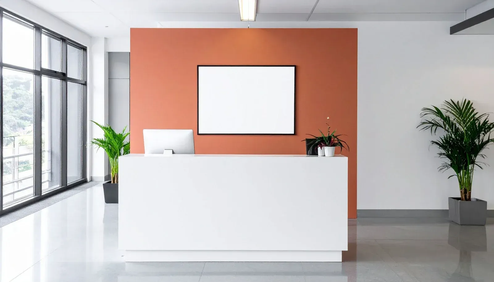 Modern white reception desk against a coral wall, blank display, indoor plants, windows.