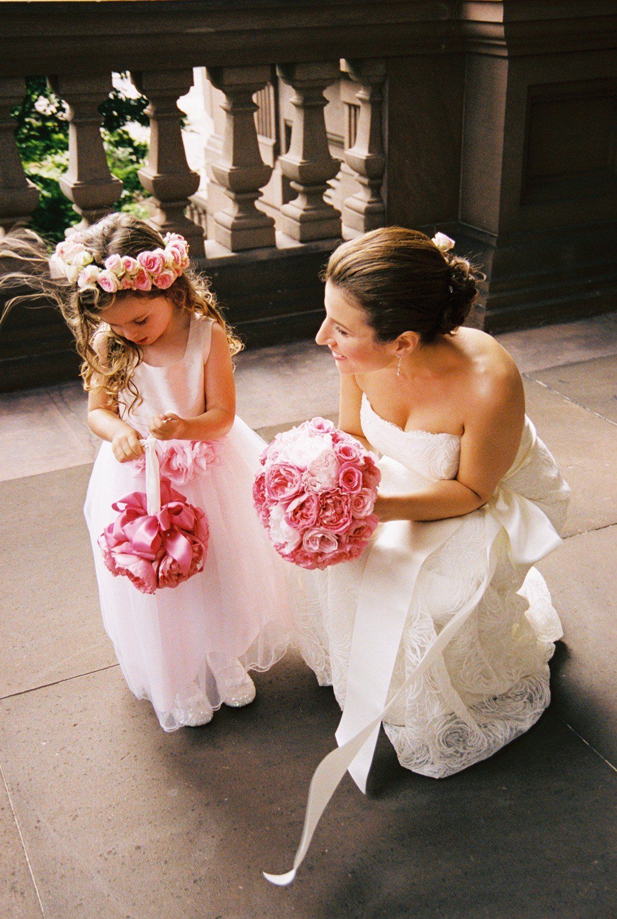 A woman in a wedding dress is kneeling down next to a flower girl