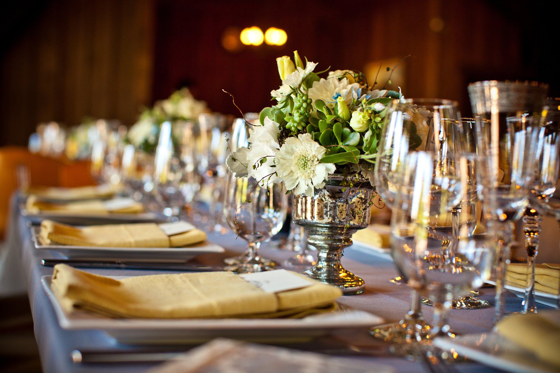 A long table with plates , wine glasses , and flowers on it.