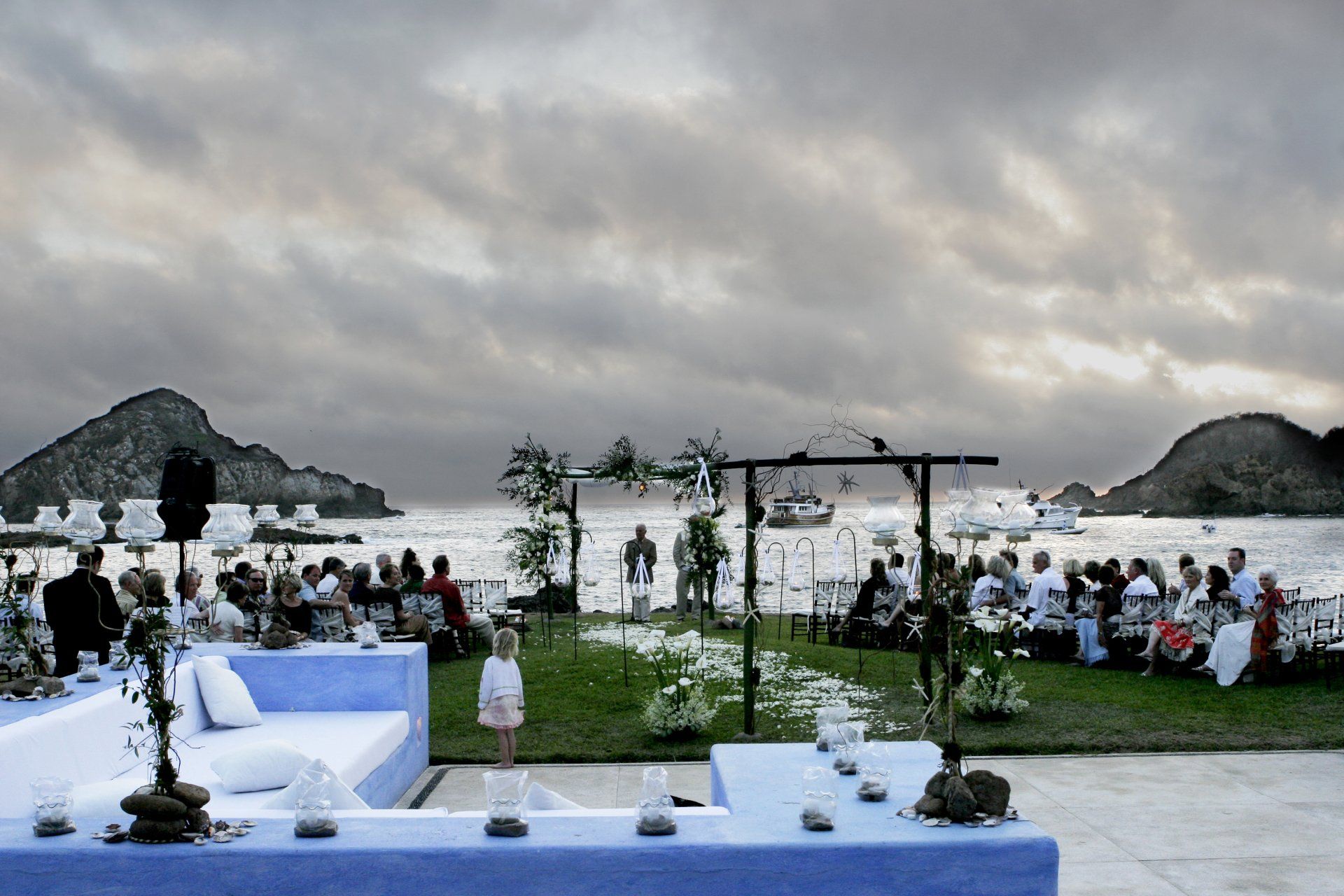 A group of people are sitting on a lawn in front of a body of water.