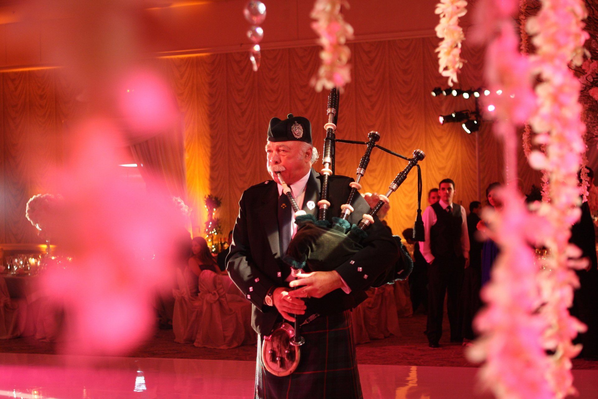 A man is playing bagpipes in a room with pink flowers hanging from the ceiling.
