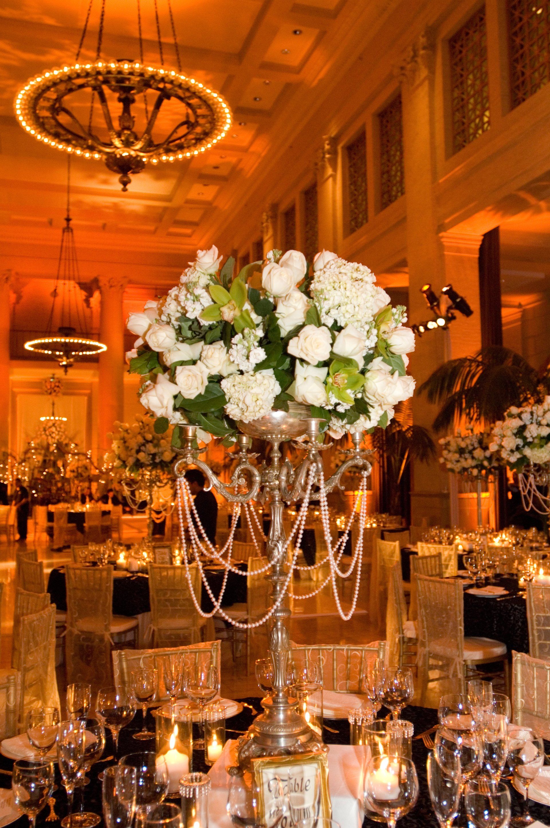 A large vase filled with white flowers sits on a table at a wedding reception.