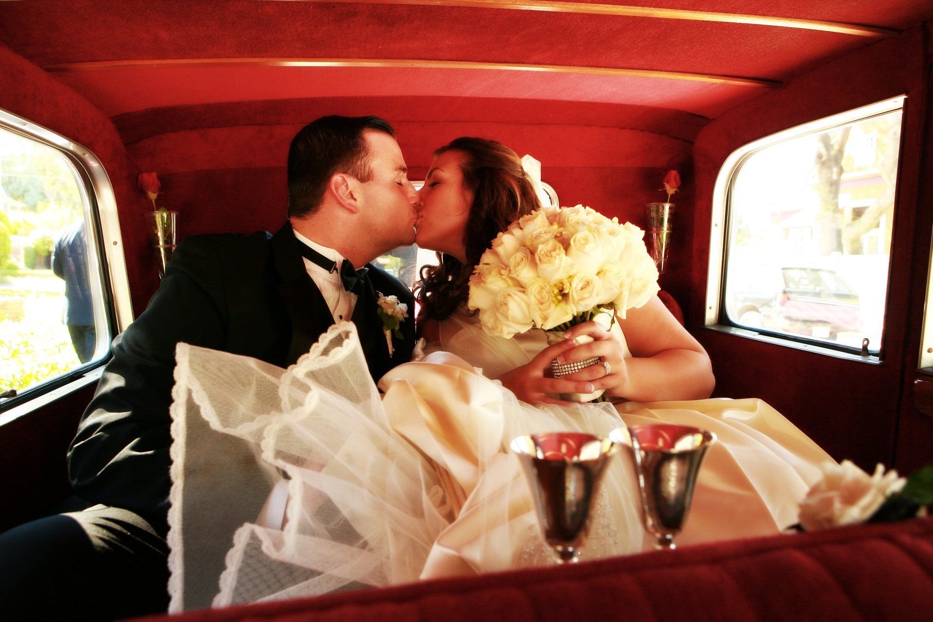 A bride and groom kissing in the back of a car