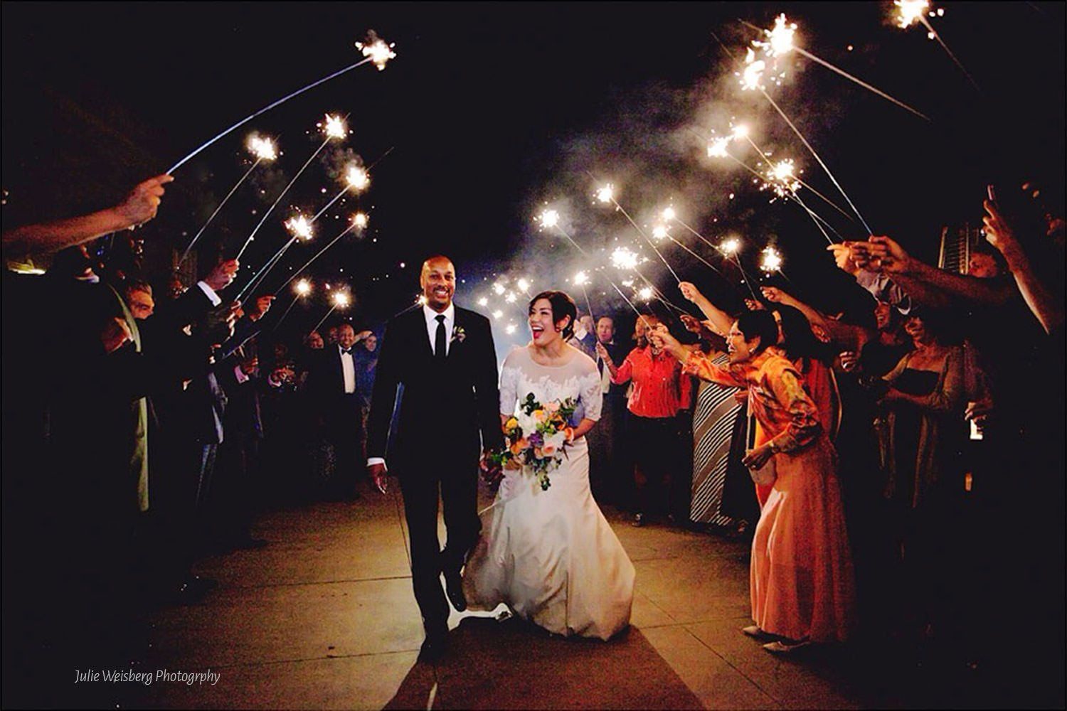 A bride and groom are walking through a tunnel of sparklers.