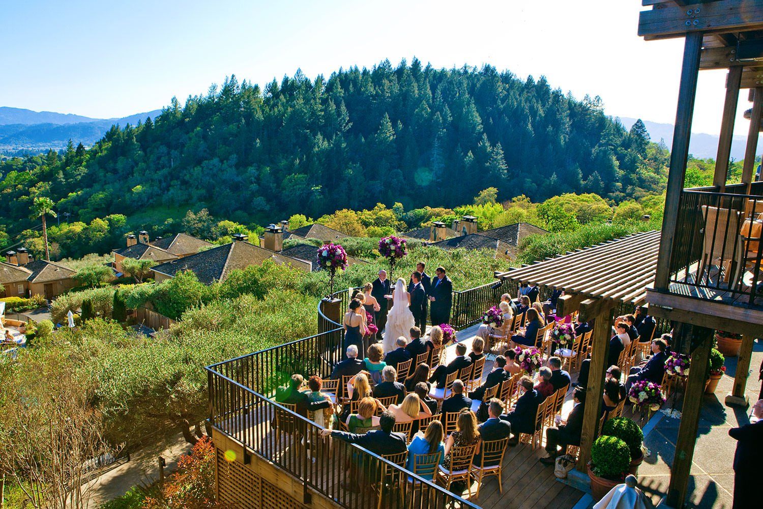 A bride and groom are getting married on a balcony overlooking a forest.