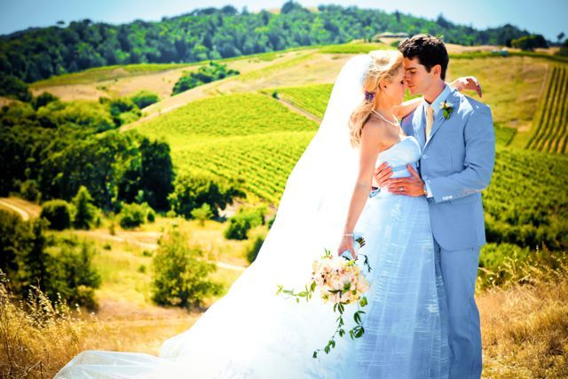 A bride and groom are kissing in front of a vineyard