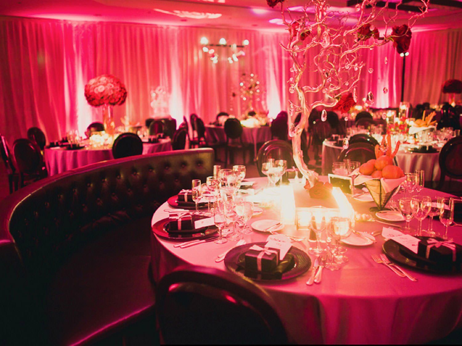 A room with tables and chairs set up for a party with pink lighting.