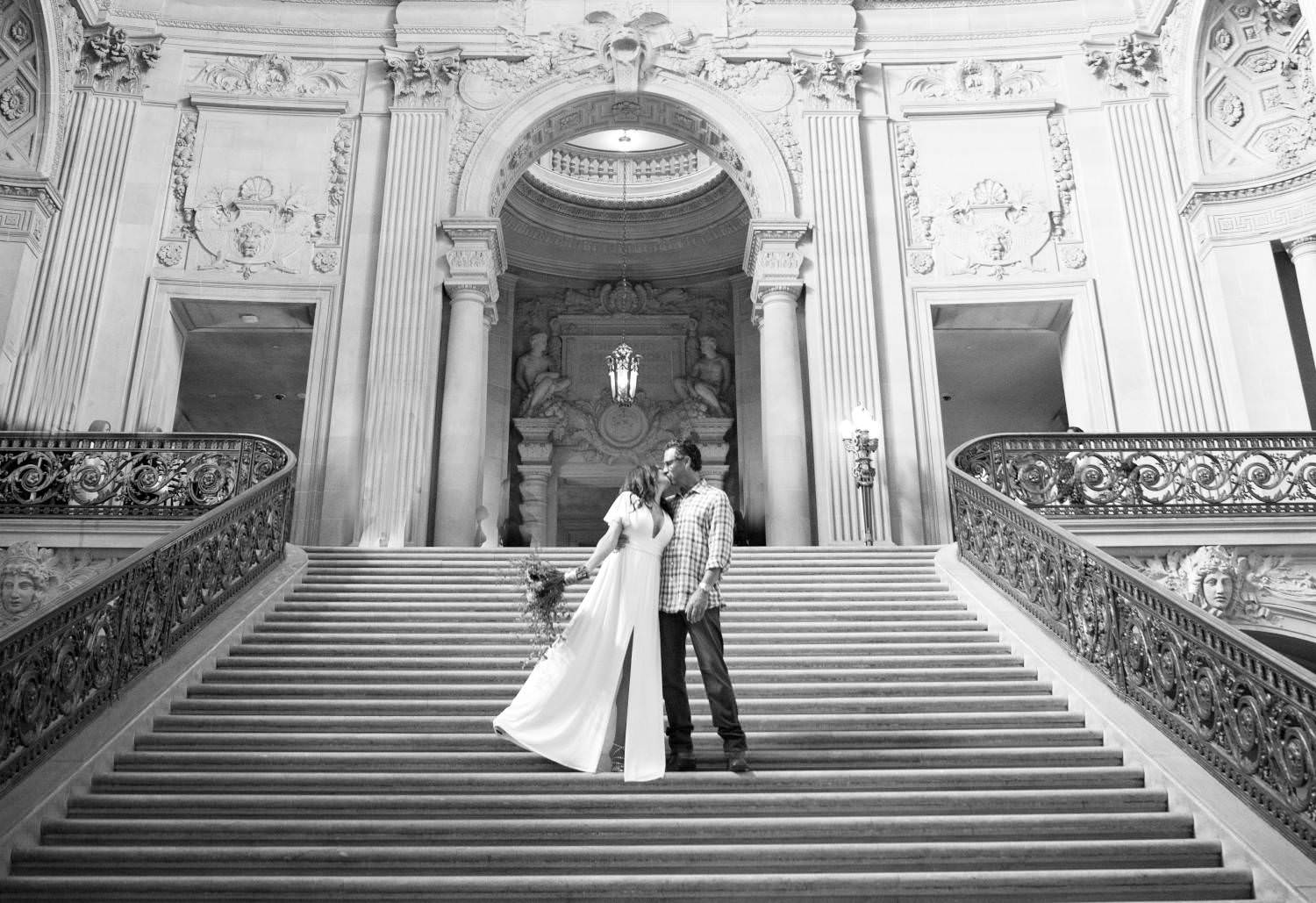 A bride and groom are standing on the stairs of a building.