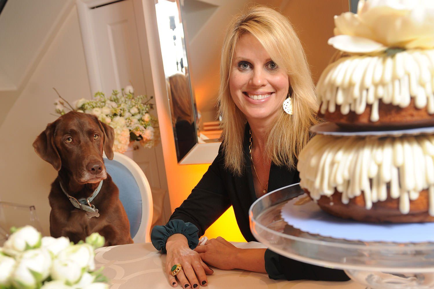 A woman and a dog are sitting at a table with a cake on it