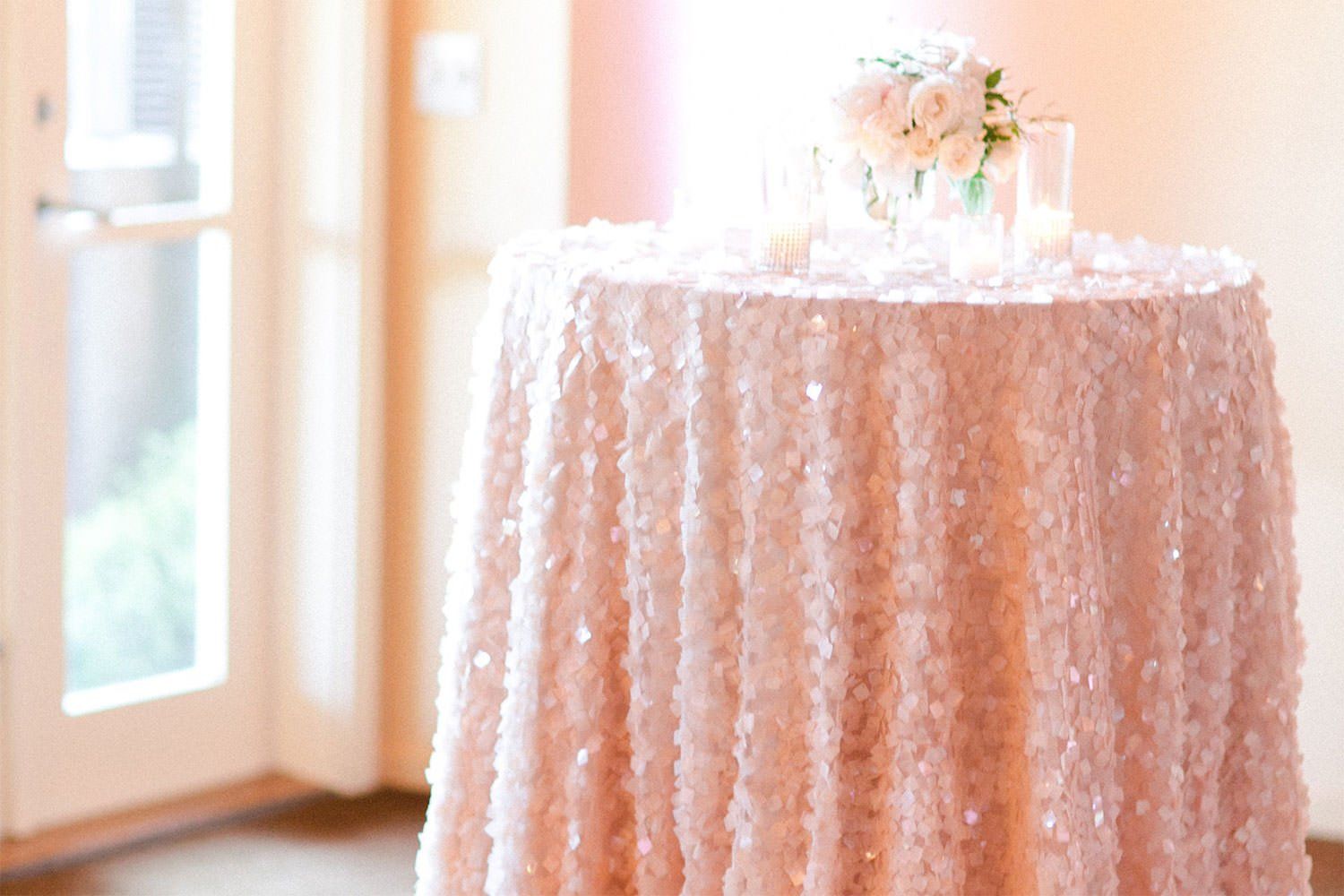 A table with a pink sequined tablecloth and a vase of flowers on it.