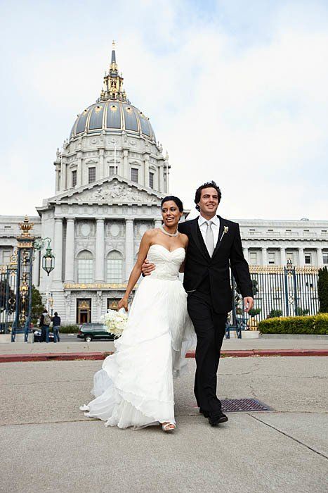 A bride and groom are walking in front of a large building.