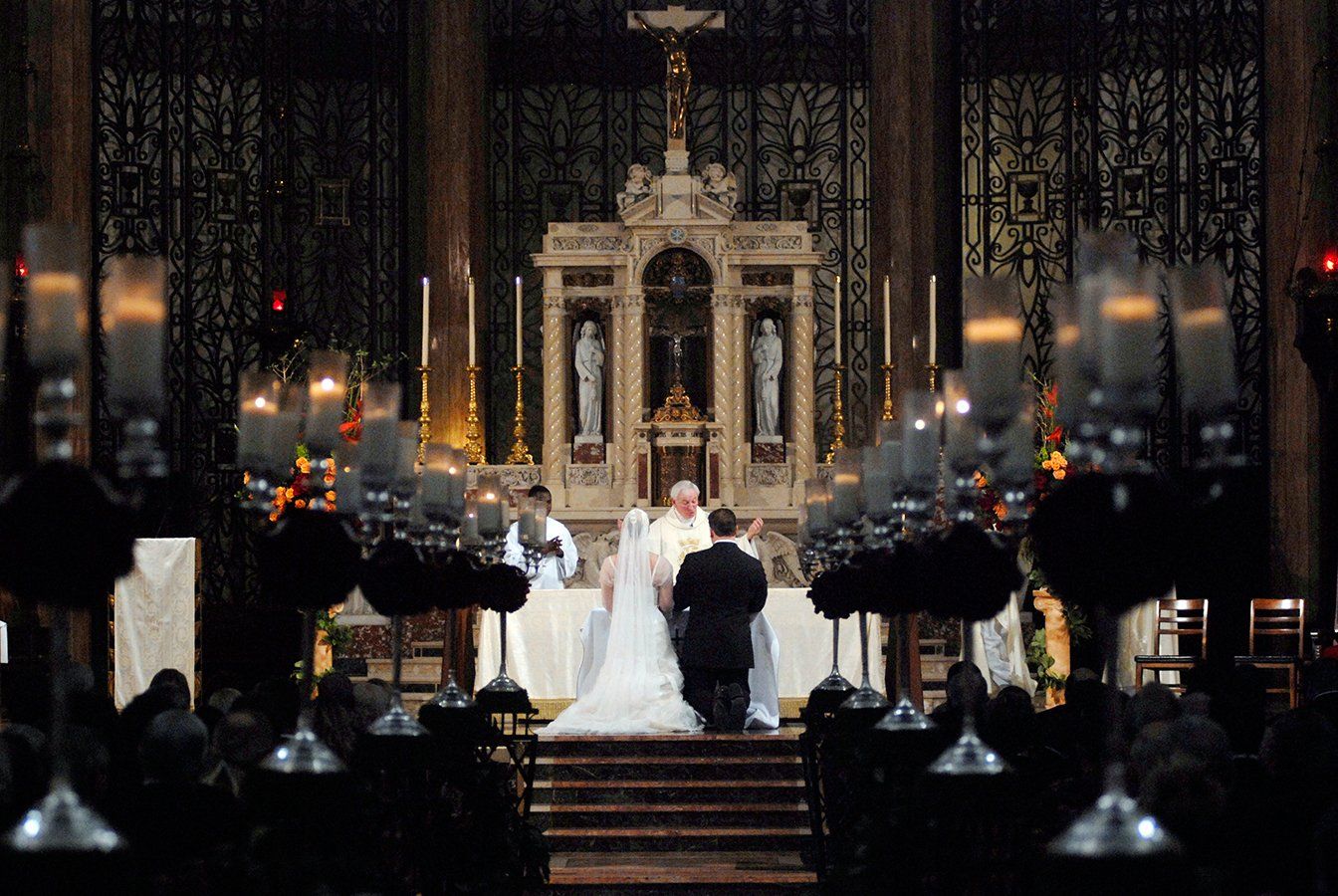 A bride and groom are kneeling in front of an altar in a church.