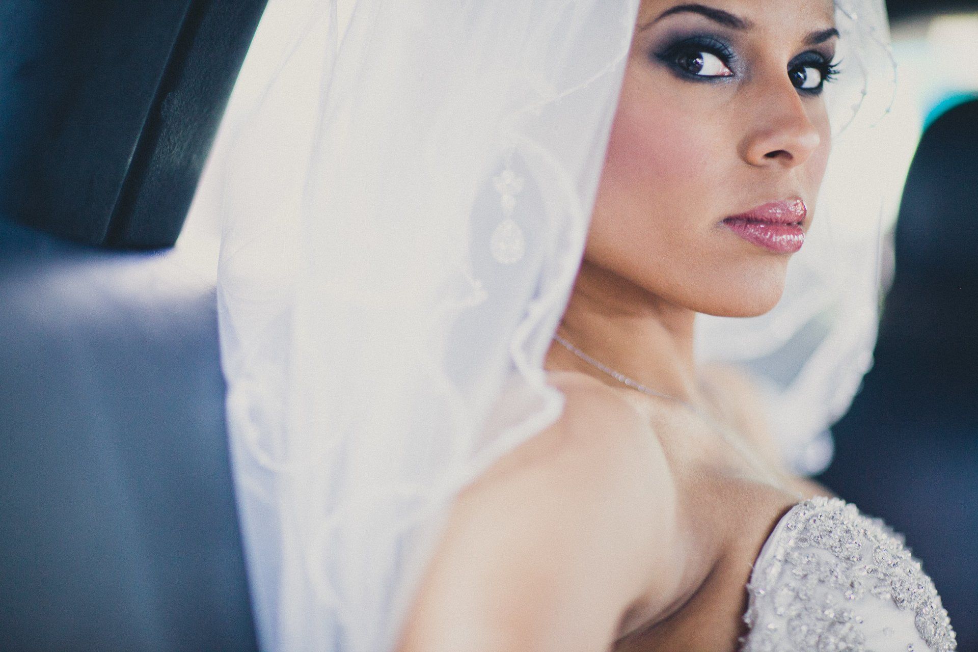 A woman in a wedding dress and veil is sitting in the back seat of a car.