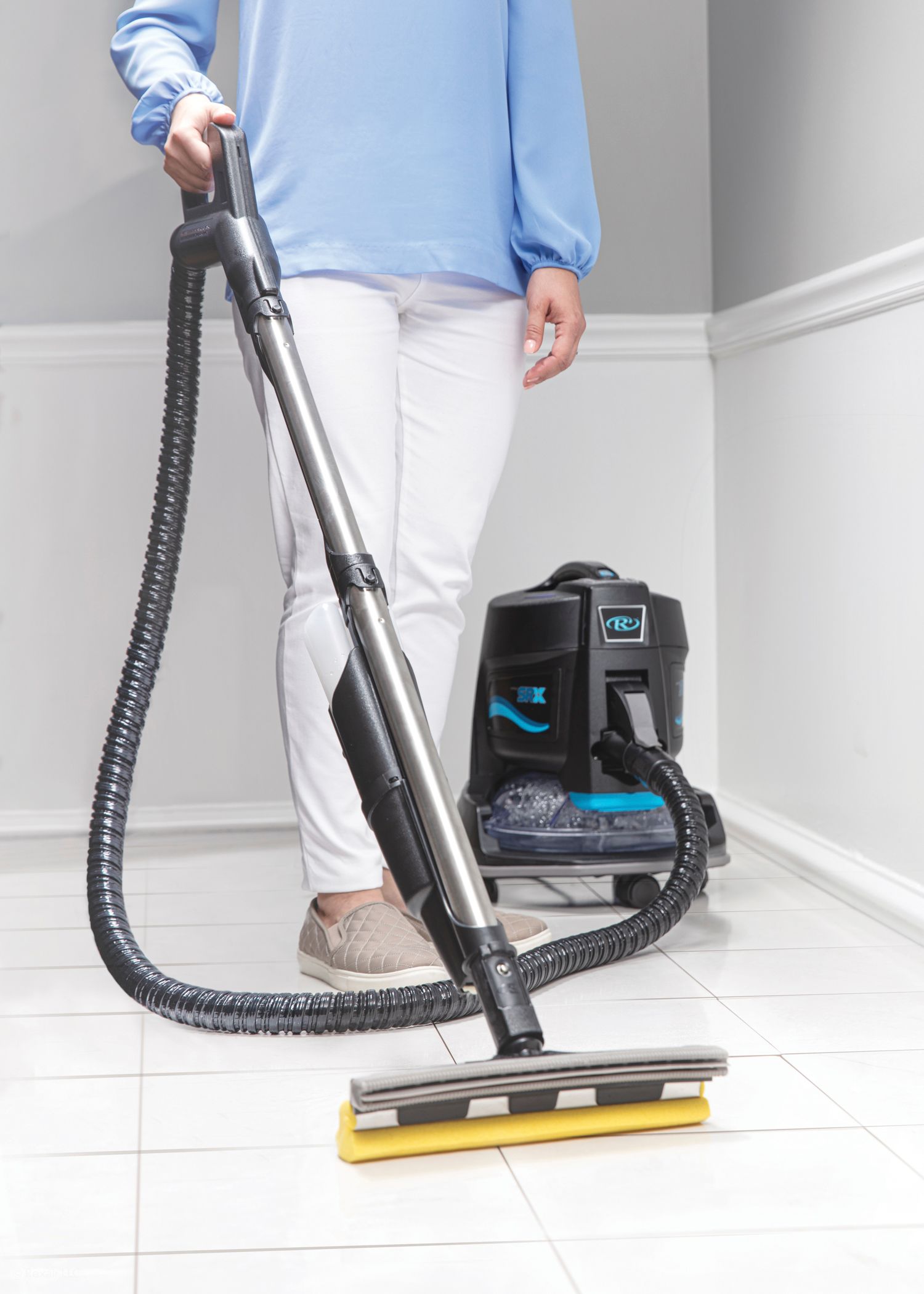 A woman is using a vacuum cleaner to clean a tiled floor.