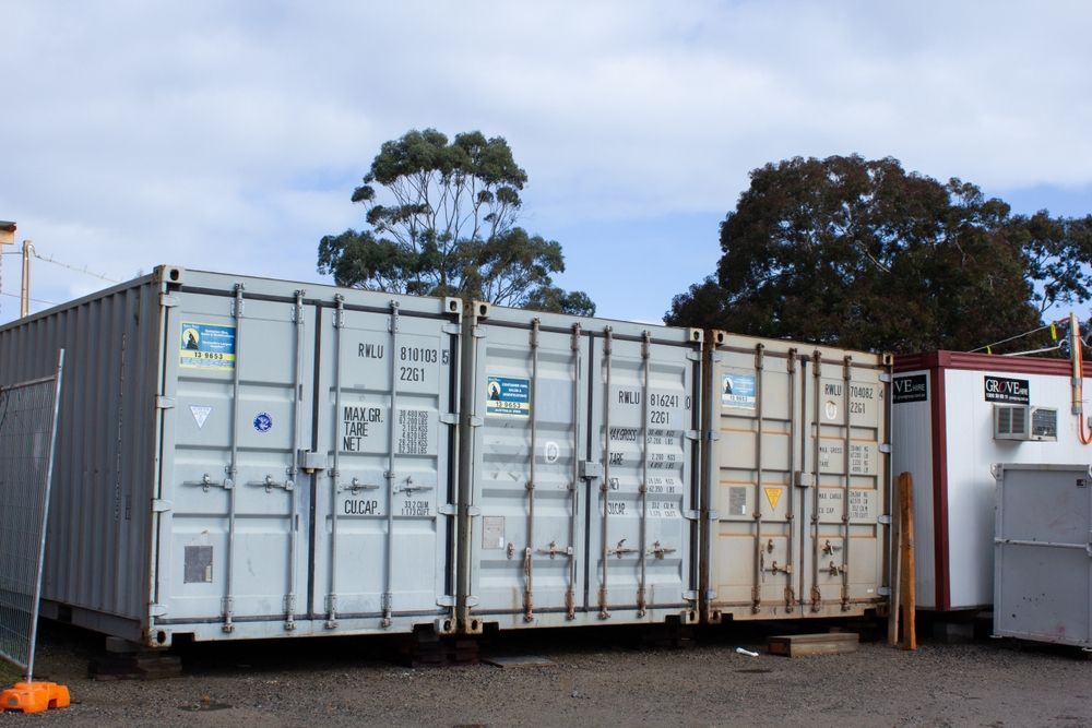 Three gray and beige shipping containers lined up outdoors, with trees in the background — Alfie's Towing in Georgetown, QLD