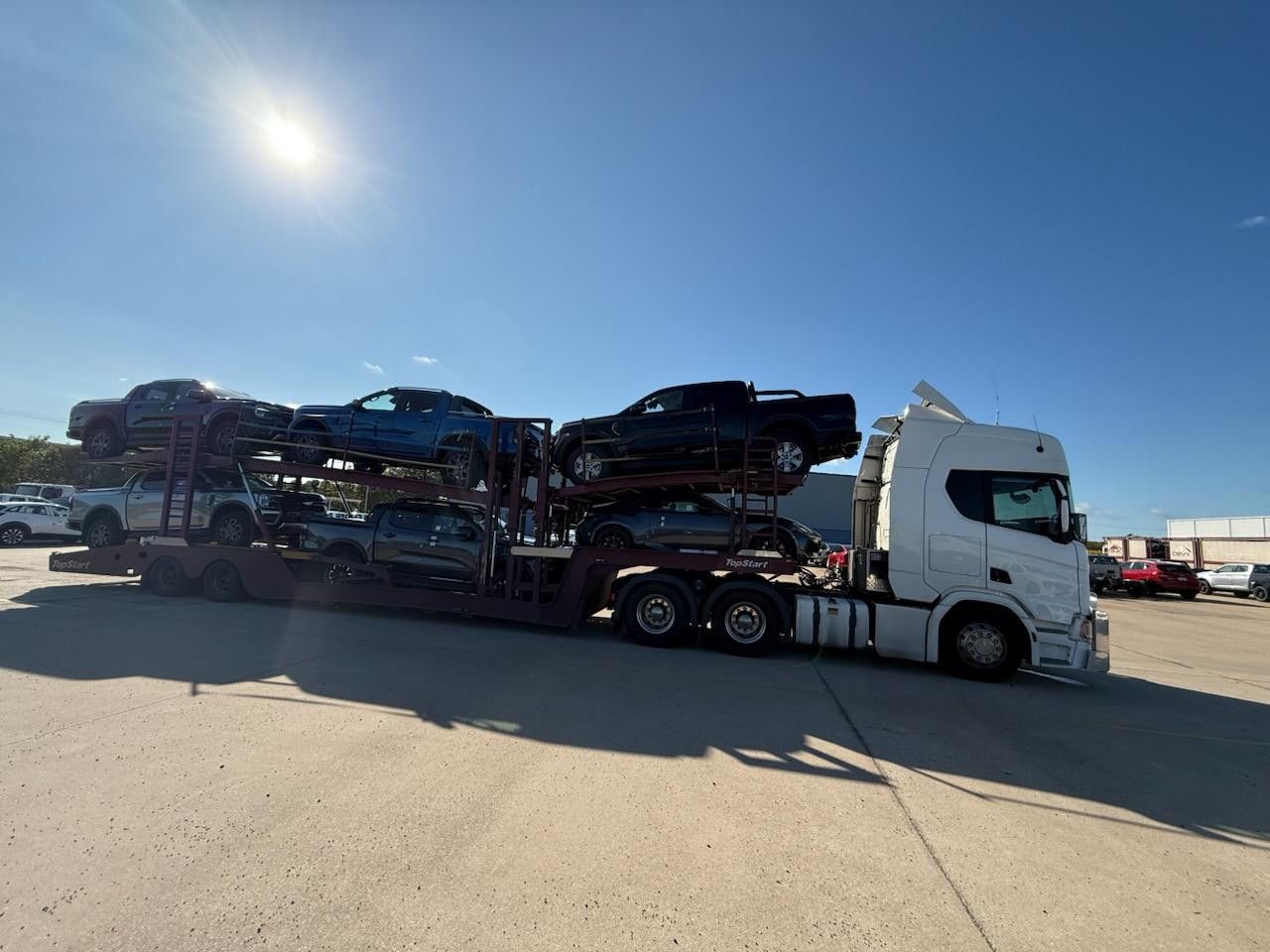 Truck Carrying Several Pickup Trucks Parked in a Lot Under a Clear Blue Sky — Alfie's Towing in Bentley Park, QLD