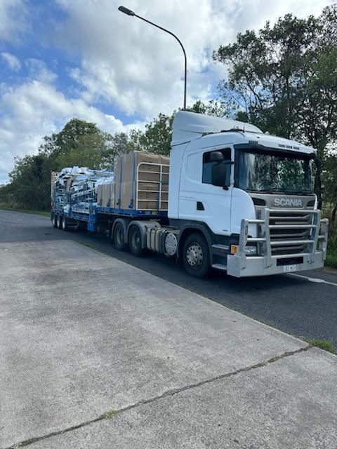 White Semi-truck With Flatbed Trailer Carrying Construction Materials — Alfie's Towing in Ravenshoe, QLD