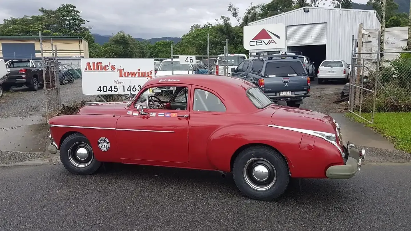 Red Vintage Car Parked in Front of a Building With a Sign and Other Vehicles Nearby — Alfie's Towing in Cooktown, QLD