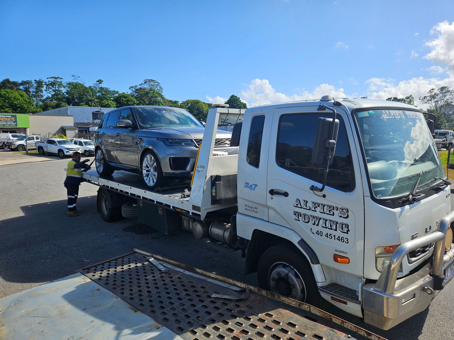 Blue Minivan on a Tow Truck, on a Road Lined With Green Trees — Alfie's Towing in Bentley Park, QLD
